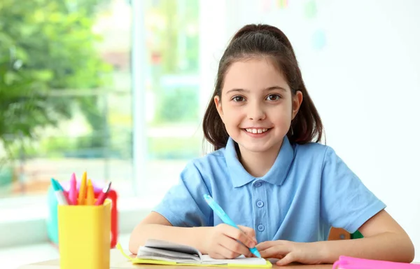 Klein meisje doet toewijzing aan Bureau in klaslokaal. School briefpapier — Stockfoto