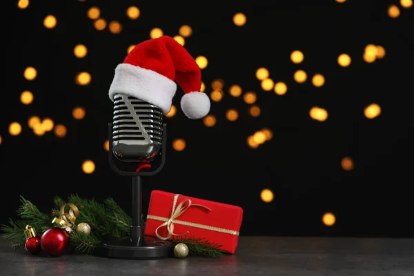 Micrófono con sombrero de Santa Claus y decoraciones en mesa gris contra luces borrosas, espacio para texto. Música navideña — Foto de Stock