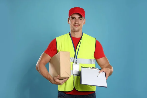 Happy young courier with parcel and clipboard on blue background — Stock Photo, Image
