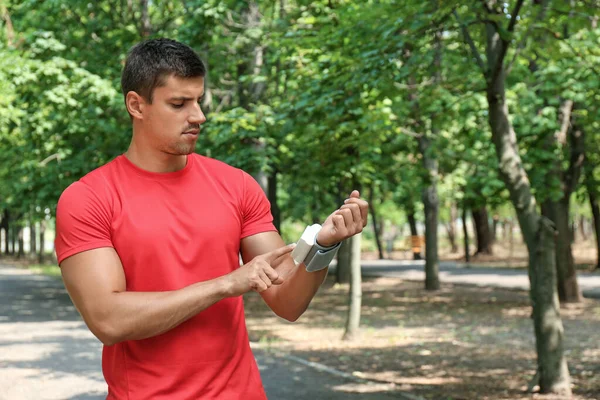 Hombre joven comprobando el pulso con dispositivo médico después del entrenamiento al aire libre — Foto de Stock