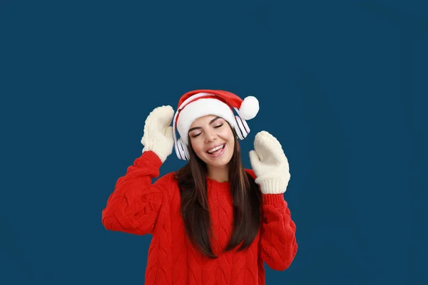 Jovem mulher em chapéu de Santa ouvindo música de Natal em fundo azul escuro — Fotografia de Stock