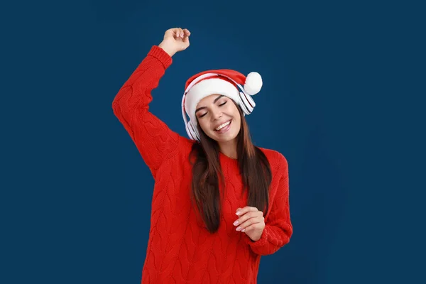 Giovane donna in cappello Santa ascoltare musica di Natale su sfondo blu scuro — Foto Stock