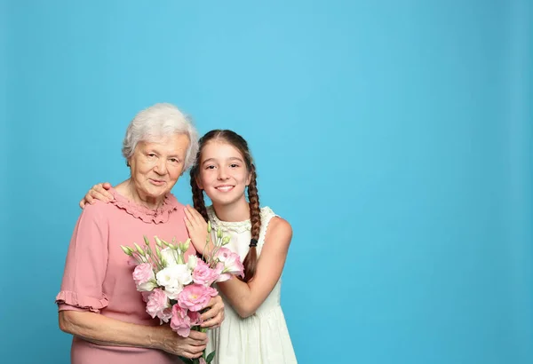 Menina bonito e sua avó com flores em fundo azul claro. Espaço para texto — Fotografia de Stock