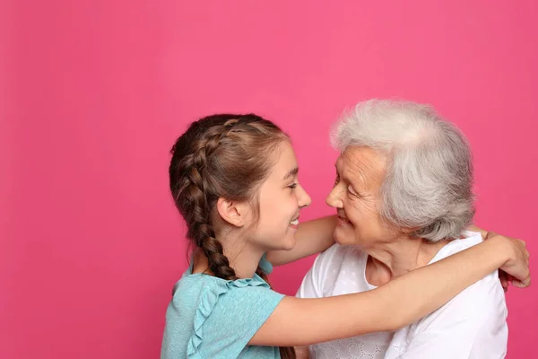 Menina bonito abraçando sua avó no fundo rosa — Fotografia de Stock