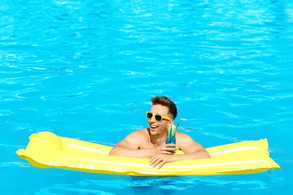 Ευτυχισμένος νέος άντρας με κοκτέιλ και φουσκωτό στρώμα στην πισίνα — Φωτογραφία Αρχείου