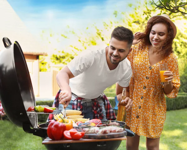 Young man and woman with drinks near barbecue grill outdoors — Stock Photo, Image