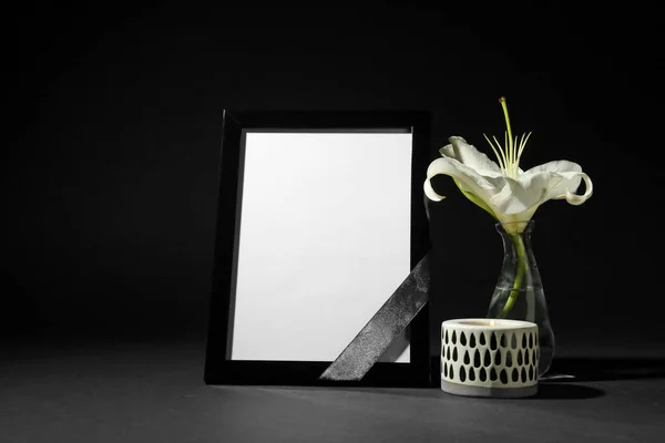 Funeral photo frame with ribbon, white lily and candle on black background. Space for design