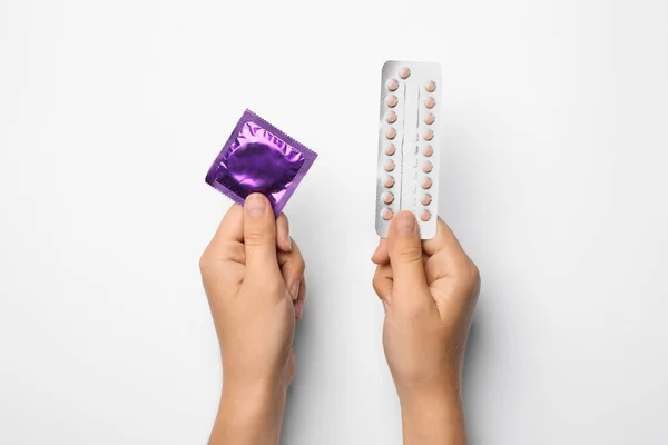 Wanita memegang kondom dan pil kontrasepsi di latar belakang putih, pandangan atas. Aman seks — Stok Foto