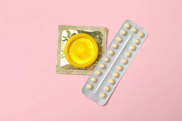 Презервативы и противозачаточные таблетки на розовом фоне, вид сверху. Безопасный секс — стоковое фото