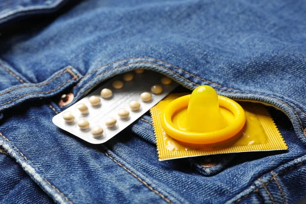 Желтые презервативы и противозачаточные таблетки в кармане джинсов, крупным планом. Безопасный секс — стоковое фото