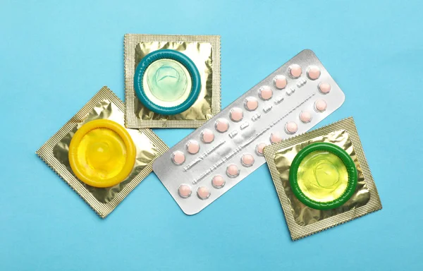 Презервативы и противозачаточные таблетки на голубом фоне, плоский уголок. Безопасный секс — стоковое фото
