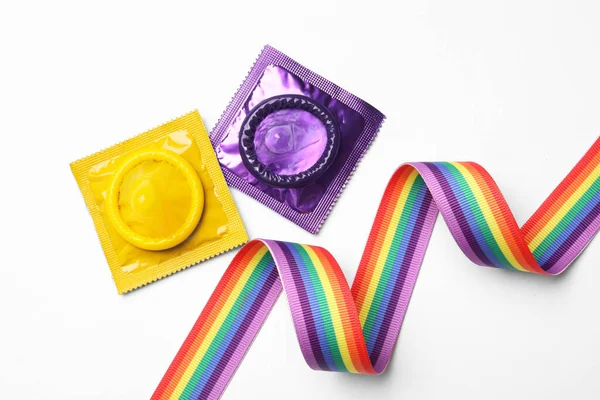 Barevné kondomy a duhová stuha na bílém pozadí, výhled shora. Koncept Lgbt — Stock fotografie