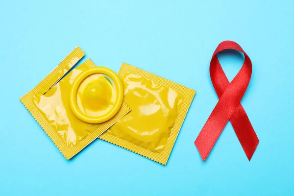 Yellow condoms and red ribbon on light blue background, flat lay. LGBT concept — Zdjęcie stockowe
