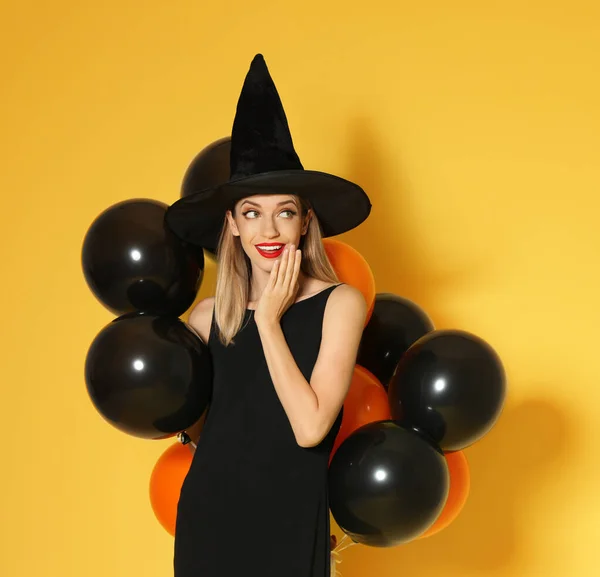 Bella donna che indossa costume da strega con palloncini per la festa di Halloween su sfondo giallo, spazio per il testo — Foto Stock