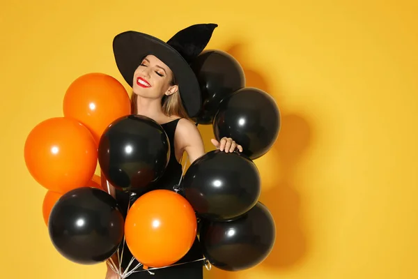 Mulher bonita vestindo traje de bruxa com balões para festa de Halloween em fundo amarelo, espaço para texto — Fotografia de Stock