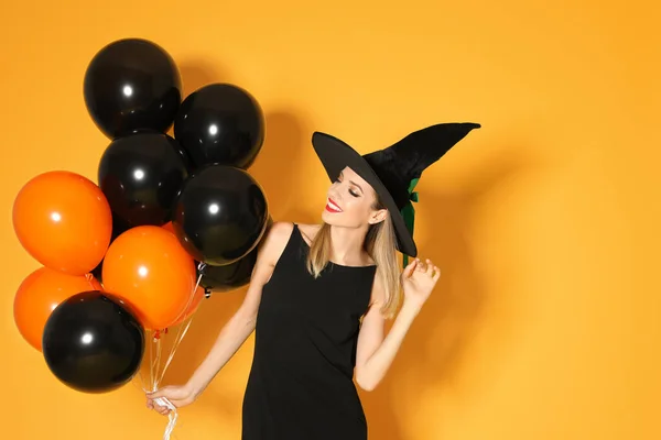 Schöne Frau trägt Hexenkostüm mit Luftballons für Halloween-Party auf gelbem Hintergrund — Stockfoto