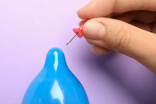 Donna piercing preservativo gonfiato con perno su sfondo viola, primo piano. Sesso sicuro — Foto Stock