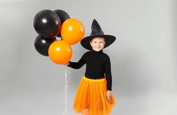 Menina bonito com balões vestindo traje de Halloween em fundo cinza — Fotografia de Stock