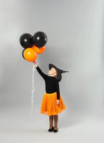 Söt liten flicka med ballonger bär Halloween kostym på grå bakgrund — Stockfoto