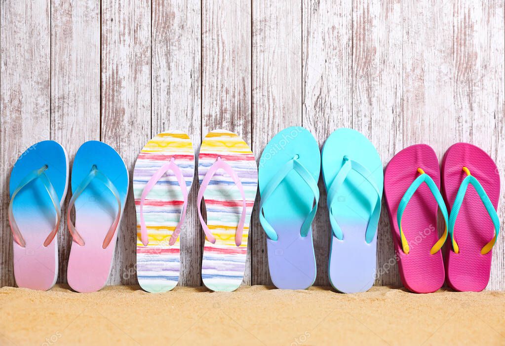 Different bright flip flops on sand near wooden wall, space for text. Summer beach accessories