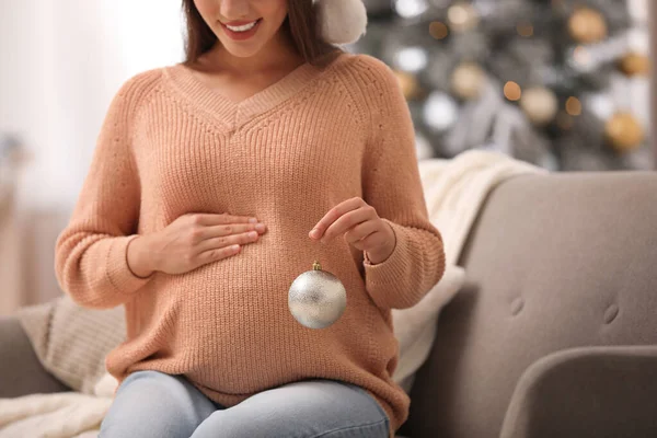 Šťastná těhotná žena s vánoční míč v obývacím pokoji, detailní záběr. Očekává se dítě — Stock fotografie