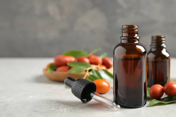 Glass bottles with jojoba oil and seeds on stone table against grey background. Space for text — Stock Photo, Image