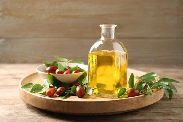 Butelka szklana z olejem jojoba i nasionami na drewnianym stole — Zdjęcie stockowe