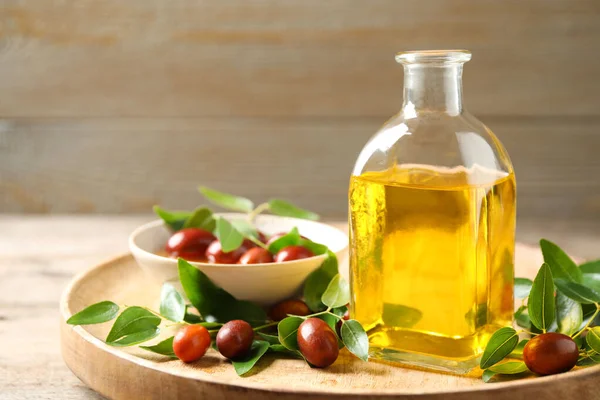 Botella de vidrio con aceite de jojoba y semillas sobre mesa de madera. Espacio para texto —  Fotos de Stock