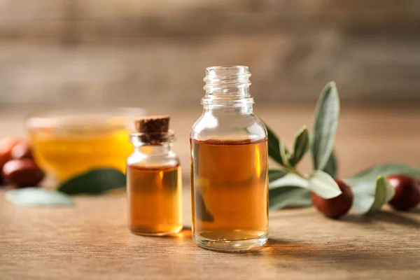 Glass bottles with jojoba oil on wooden table