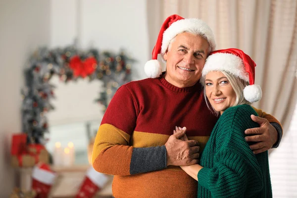 Feliz casal maduro em chapéus de Santa em casa. Celebração de Natal — Fotografia de Stock