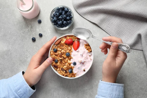 Woman eating tasty homemade granola with yogurt and berries at grey table, top view. Healthy breakfast — Stock Photo, Image