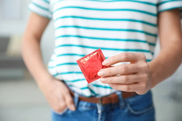 Kvinnan håller kondom inomhus, närbild. Säkert sex koncept — Stockfoto