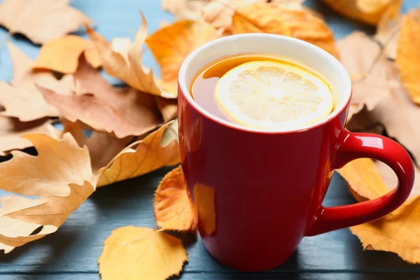 Xícara de bebida quente e folhas na mesa de madeira azul. Atmosfera de outono acolhedor — Fotografia de Stock