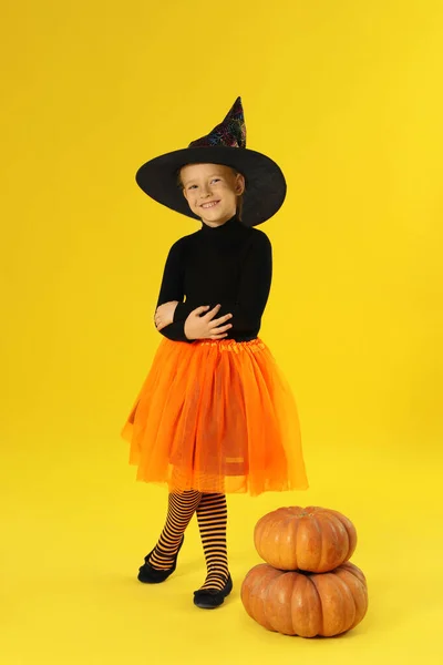 Menina bonito com abóboras vestindo traje de Halloween no fundo amarelo — Fotografia de Stock