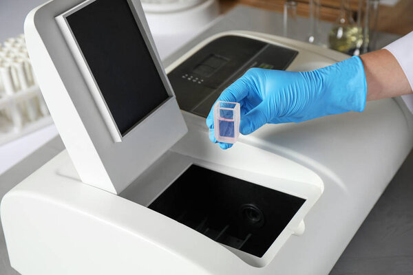 Scientist putting sample compartment with liquid in spectrophotometer, closeup. Laboratory analysis
