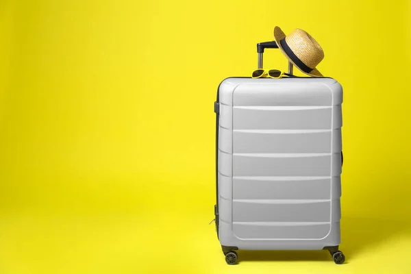 Elegante maleta gris con sombrero y gafas de sol sobre fondo amarillo. Espacio para texto — Foto de Stock