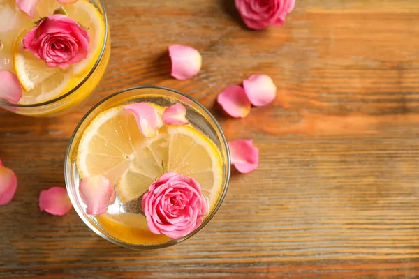 Tasty refreshing lemon drink with roses on wooden table, flat lay — Stock Photo, Image