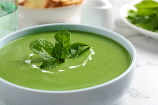 Bowl of healthy green soup with fresh spinach on marble table, closeup view