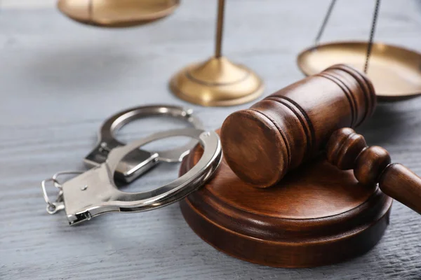 Молоток, наручники и весы правосудия на сером деревянном столе, крупный план. Уголовное право — стоковое фото