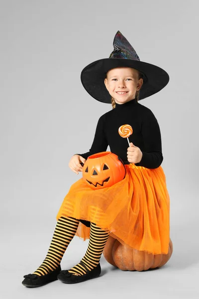 Schattig klein meisje met pompoen snoep emmer en lolly dragen Halloween kostuum op grijze achtergrond — Stockfoto