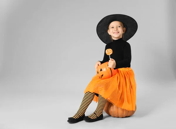 Cute little girl z dyni wiadro cukierki i lizak noszenie kostium Halloween na szarym tle. Miejsce na tekst — Zdjęcie stockowe