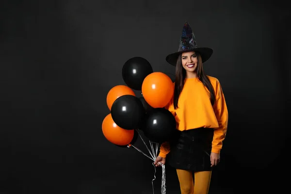 Hermosa mujer con traje de bruja con globos para la fiesta de Halloween sobre fondo negro, espacio para el texto —  Fotos de Stock