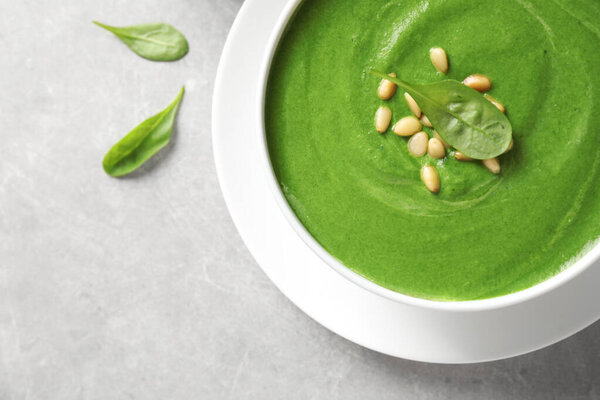 Bowl with fresh green healthy spinach soup on grey table, top view. Space for text