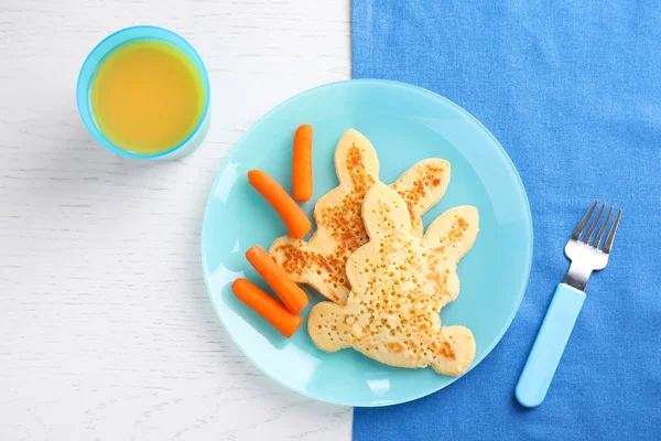 Pancake berbentuk kelinci yang lezat disajikan dengan wortel dan jus di atas meja kayu putih, berbaring datar. Ide kreatif untuk sarapan anak-anak — Stok Foto