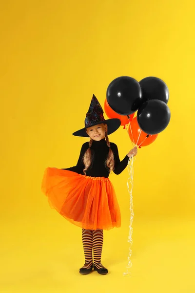 Carino bambina con palloncini indossando costume di Halloween su sfondo giallo — Foto Stock