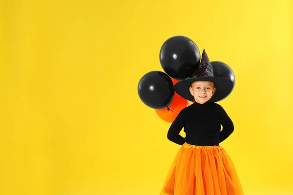 Söt liten flicka med ballonger bär Halloween kostym på gul bakgrund. Plats för text — Stockfoto