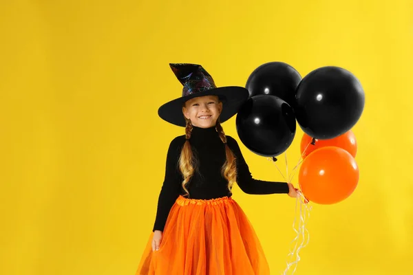 Carino bambina con palloncini indossando costume di Halloween su sfondo giallo — Foto Stock