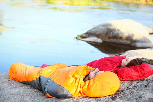 Junges Paar ruht in Schlafsäcken auf Klippe in der Nähe des Sees — Stockfoto