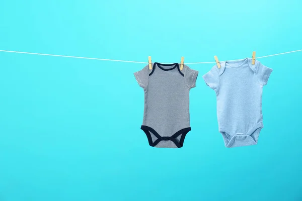 Onesies bebê colorido pendurado na linha de roupas contra fundo azul, espaço para texto. Dia de lavandaria — Fotografia de Stock