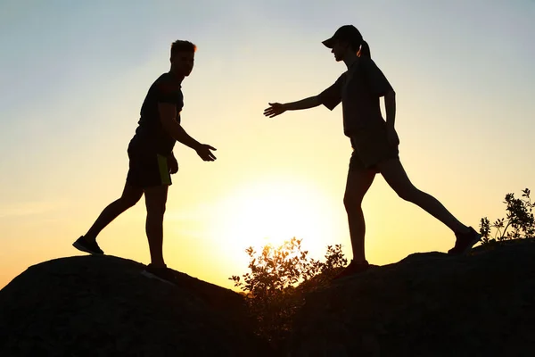 Wandelaar helpt vriend buitenshuis bij zonsondergang. Help en ondersteuning concept — Stockfoto